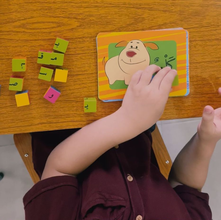 A primary schooler learning Arabic with blocks of letters to create the word seen on a card. 